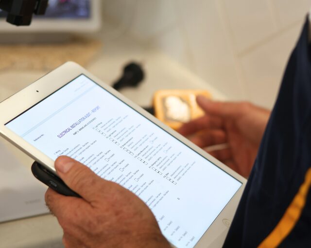 Electrician reviewing a written test report on a tablet at the switchboard